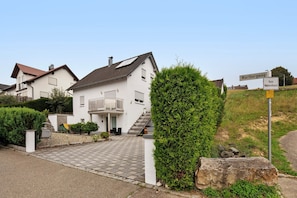 Un immeuble résidentiel avec une allée pavée, un escalier menant à l’entrée et une plaque indiquant le nom de la rue, « Wartbergweg ».