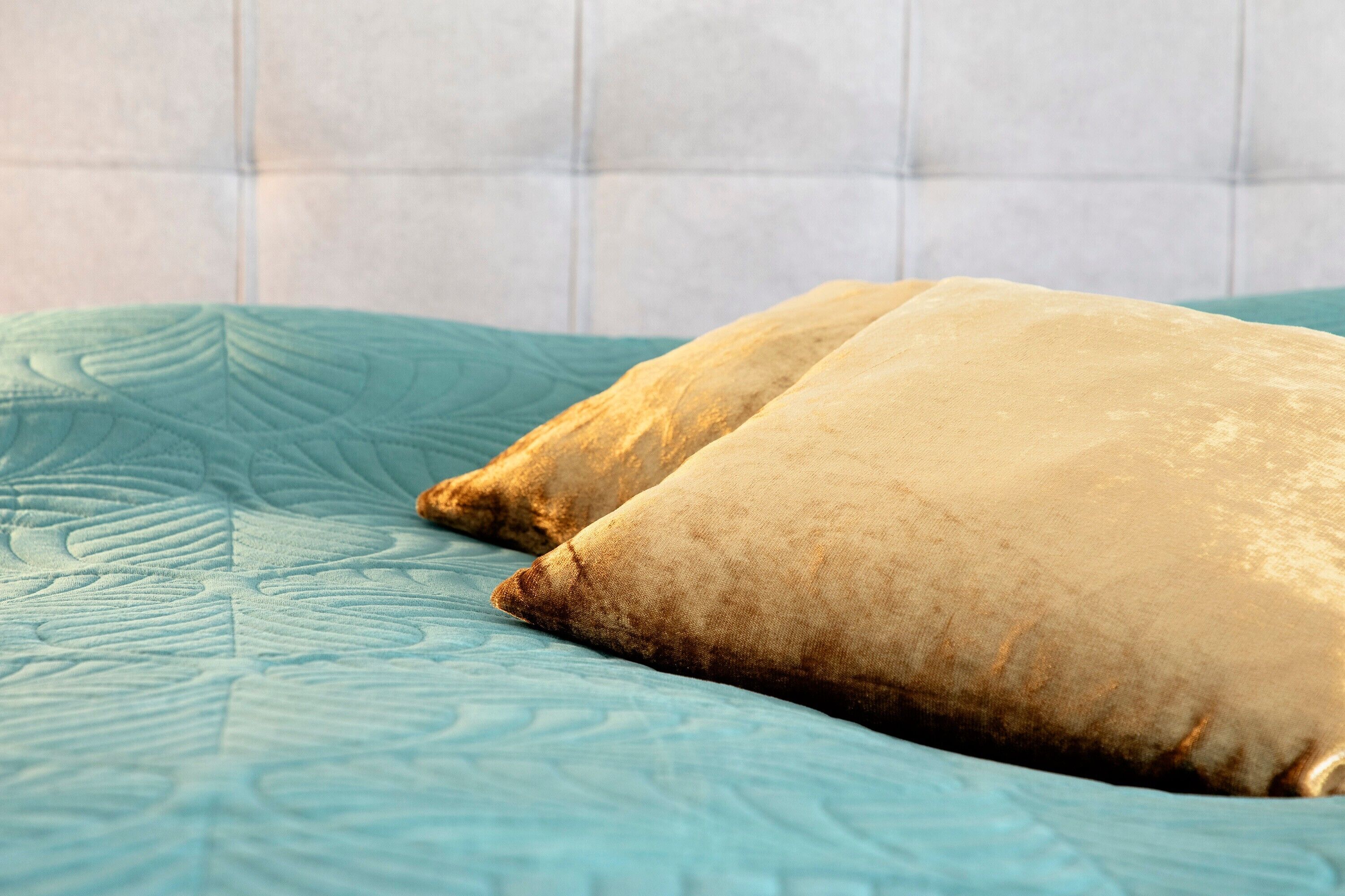 Un letto con una coperta verde acqua e due cuscini color beige.