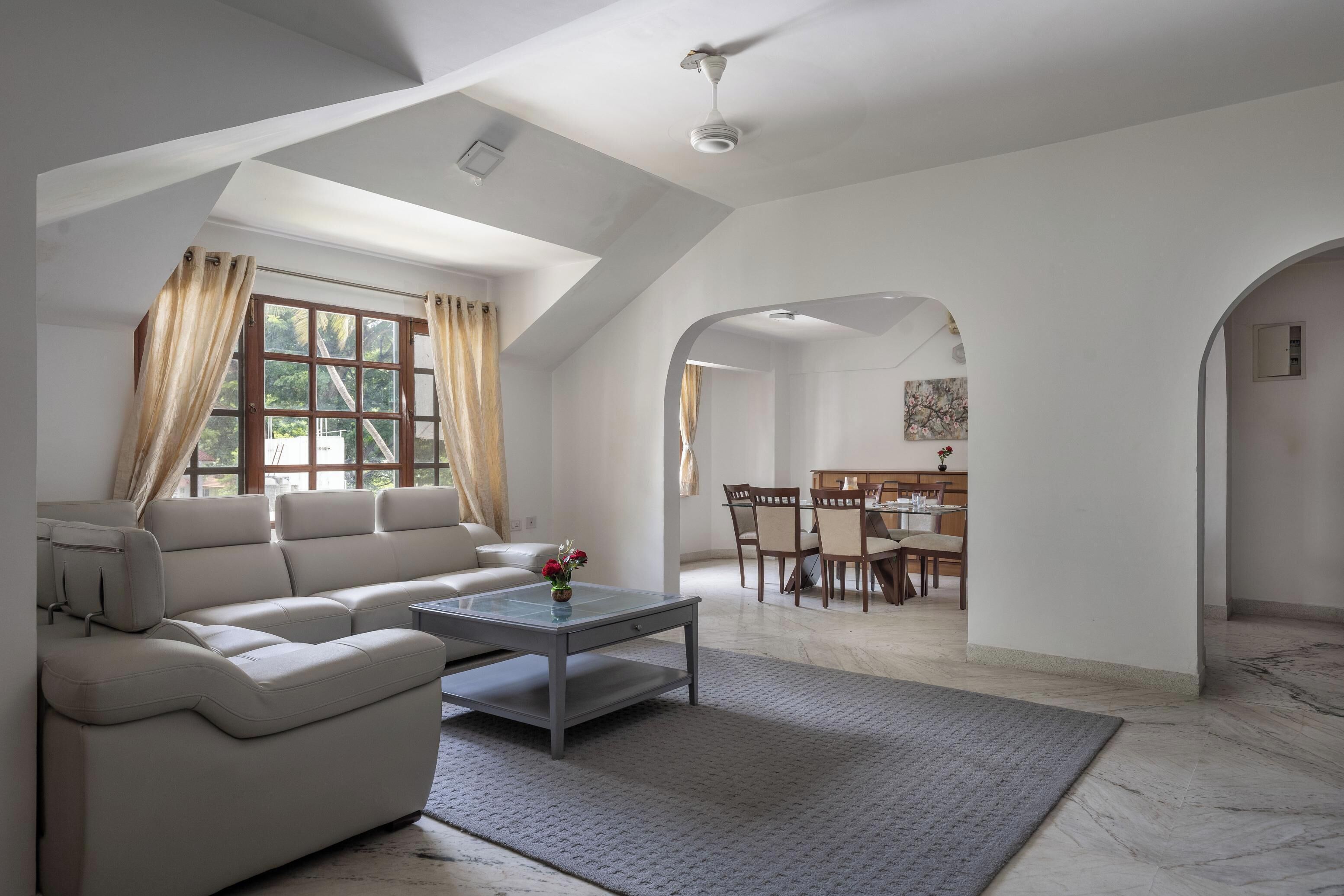A modern living room with a sectional sofa, a glass coffee table, and a dining area with a wooden table and chairs.