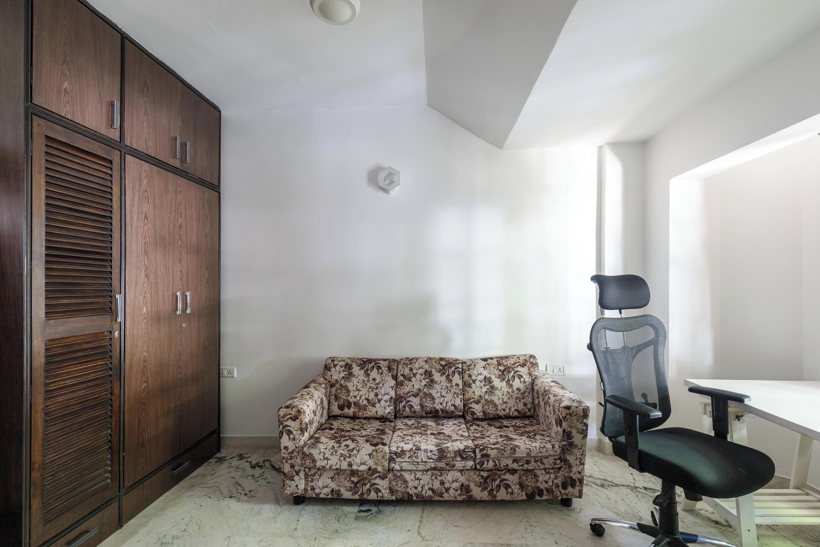 Een kamer met een houten garderobe, een bloemenbank en een zwarte bureaustoel.