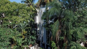 A white building surrounded by lush greenery, including palm trees and other tropical plants. - Casa Bianca by Red Olivenr Taj MG Roadpvt Garden (Bengaluru)