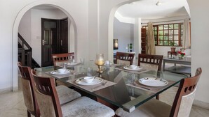 A dining area with a glass table, wooden chairs, and a chandelier. - Casa Bianca by Red Olivenr Taj MG Roadpvt Garden (Bengaluru)