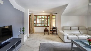 A modern living room with a flat-screen TV, a sofa, a coffee table, and a window with curtains. - Casa Bianca by Red Olivenr Taj MG Roadpvt Garden (Bengaluru)