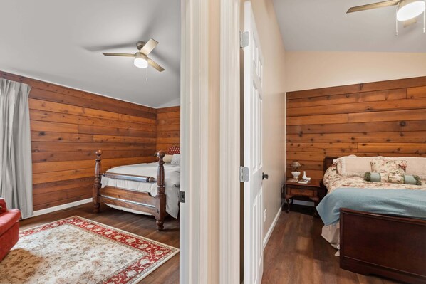 A bedroom with wooden paneling, a bed with a floral bedspread, a nightstand with a lamp, and a ceiling fan.