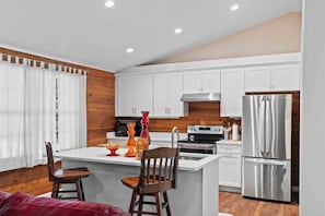 A modern kitchen with white cabinets, stainless steel appliances, and a wooden accent wall.