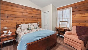 A bedroom with a wooden headboard, a bed with floral bedding, a nightstand with a lamp, a chair, and a sewing machine.