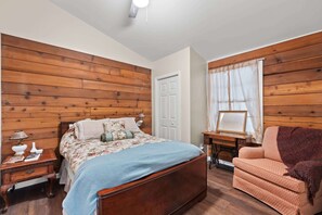 A bedroom with a wooden headboard, a bed with floral bedding, a nightstand with a lamp, a chair, and a sewing machine. - Little Birds Nest (Highlands)