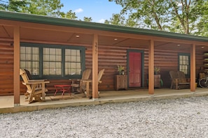 A wooden cabin with a covered porch, two wooden chairs, a small table, and a red door. - Little Birds Nest (Highlands)