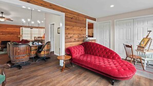 A room with a red sofa, wooden barrel chairs, a small round table, and a ceiling fan.