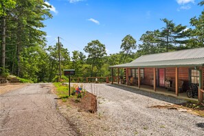 A rustic lodge with a covered porch, a gravel driveway, and a sign indicating a room number. - Little Birds Nest (Highlands)