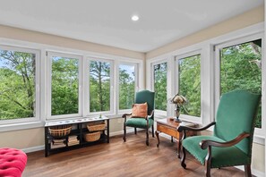 A room with large windows, a green armchair, a wooden desk, and a red ottoman. - Little Birds Nest (Highlands)