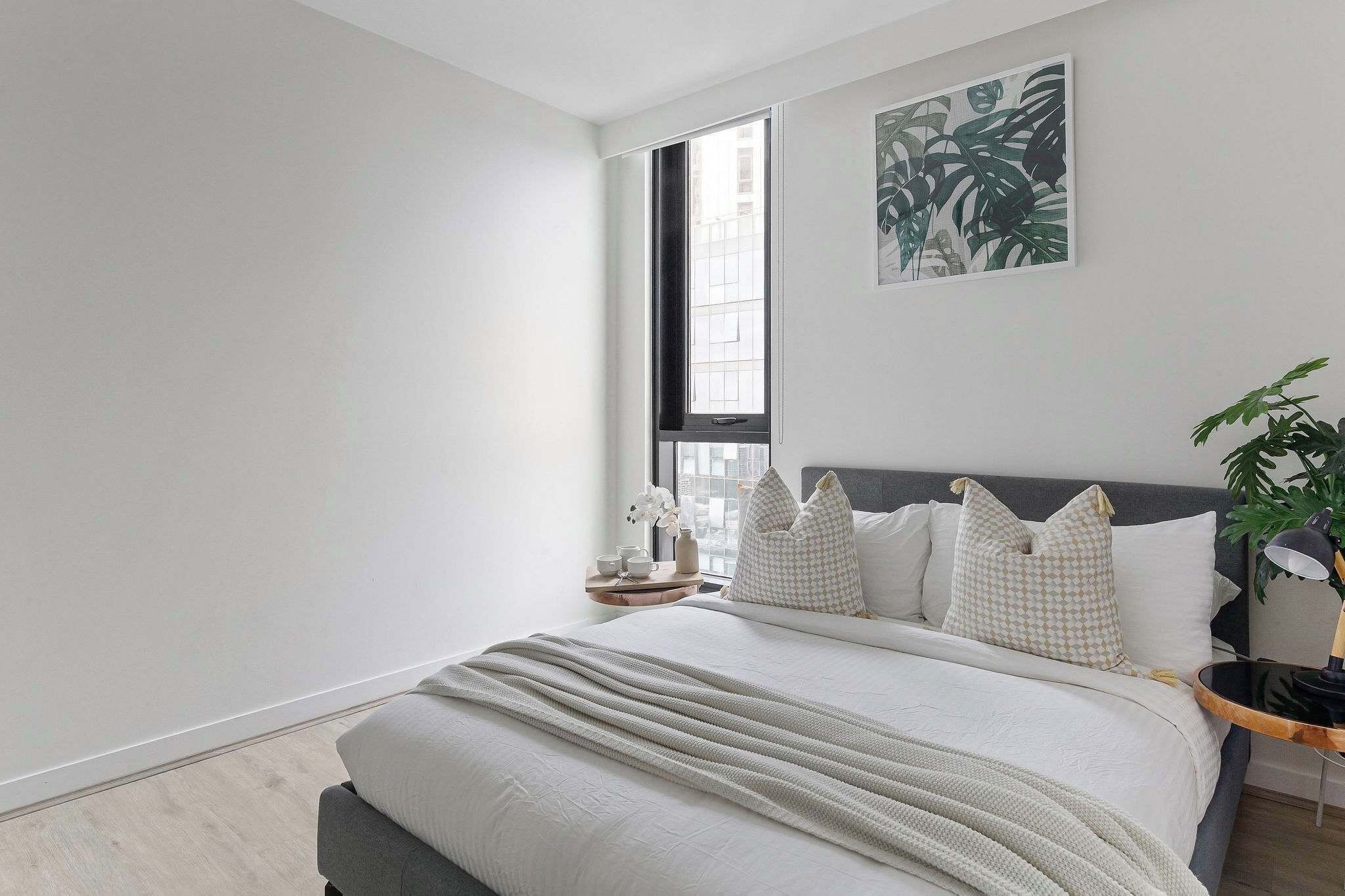 Une chambre à coucher moderne avec un grand lit, une fenêtre, une table de chevet avec une lampe et une plante.