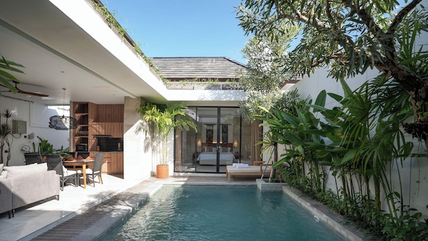 A modern outdoor pool area with a dining set and a bedroom visible through a glass door. - Deo Villa Seminyak (Seminyak)