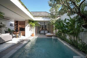 A modern outdoor pool area with a dining set and a bedroom visible through a glass door. - Deo Villa Seminyak (Seminyak)