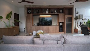 A modern living room with a grey sofa, wooden entertainment unit, ceiling fans, and a large flat-screen TV. - Deo Villa Seminyak (Seminyak)