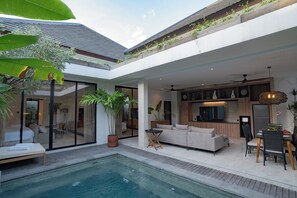 A modern outdoor living area with a pool, a sofa, and a dining table. - Deo Villa Seminyak (Seminyak)