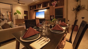 A dining area with a wooden table set for four, including plates, cutlery, and glasses. A television is mounted on the wall above the table. - Deo Villa Seminyak (Seminyak)
