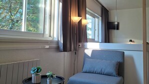 A modern room with a grey sofa, a small table with plants, a window with curtains, and a flat-screen TV mounted on the wall.