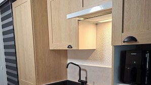 A compact kitchen with wooden cabinets, a black sink, and a built-in dishwasher.