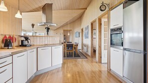 A kitchen with wooden cabinets, a stainless steel refrigerator, and a dining area with a table and chairs.