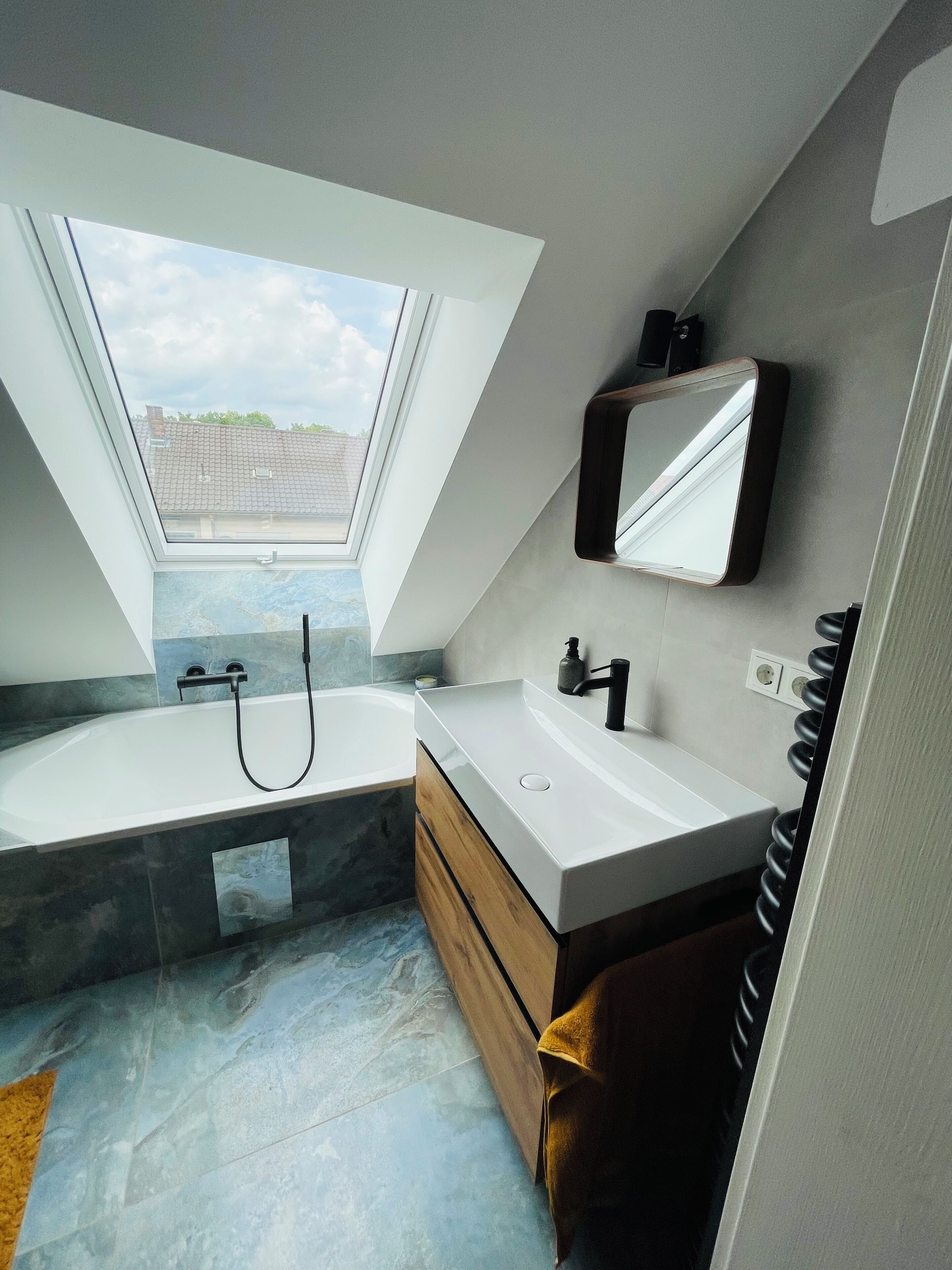 Ein modernes Badezimmer mit Oberlicht, einer Badewanne, einem Waschbecken mit Spiegel und einem Handtuchhalter.