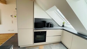 A modern kitchen with white cabinetry, a black microwave, a coffee maker, and an oven. There is a skylight above the counter. - Vacation in the Franconian Lake District. Modern and light-flooded apartment. (Allersberg)