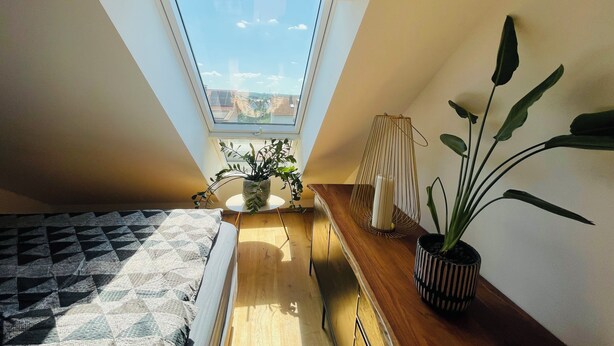 A bedroom with a skylight, a bed, a bedside table with a plant, and a small table with a candle. - Vacation in the Franconian Lake District. Modern and light-flooded apartment. (Allersberg)