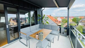 A modern balcony with a grey sofa, wooden table, and potted plants. - Vacation in the Franconian Lake District. Modern and light-flooded apartment. (Allersberg)