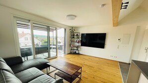 A modern living room with a grey sofa, wooden coffee table, and a flat-screen TV mounted on the wall. - Vacation in the Franconian Lake District. Modern and light-flooded apartment. (Allersberg)