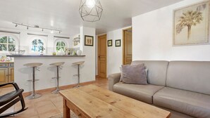 Une cuisine moderne avec des tabourets de bar, une table en bois et un canapé dans un espace de vie lumineux, agrémenté d’un luminaire au plafond.