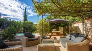 Un espace extérieur aménagé avec des meubles en osier, une piscine et une pergola offrant de l’ombre.