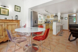 Una cocina moderna con comedor, que incluye una mesa redonda de vidrio, sillas rojas y transparentes, y un armario de madera.