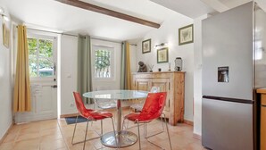 Une cuisine équipée d’un réfrigérateur, d’une table à manger avec des chaises, d’un buffet en bois et d’une fenêtre avec des rideaux.