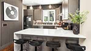 A modern kitchen with a large island, bar stools, pendant lighting, and a vinyl record on the wall. - New 1.5 Miles to Broadway | City Views | Game Room (Nashville)