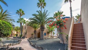 A pathway leading to a building with a staircase, surrounded by palm trees and a clear sky. - Oasis Duna 'Casa Martineli' with Shared Pool, Balcony, and Wi-Fi (Corralejo)