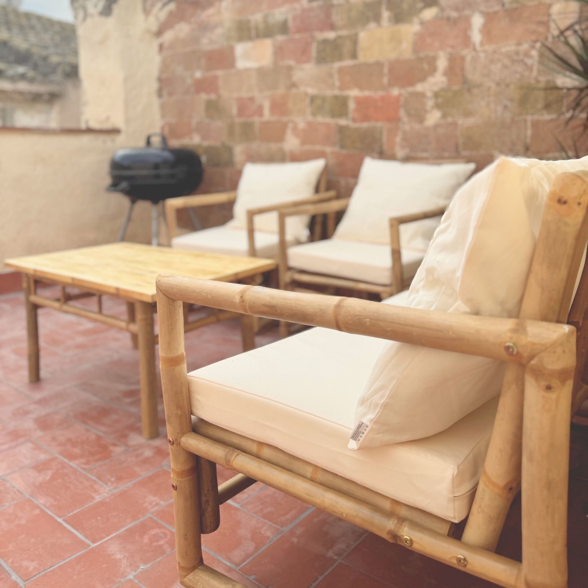 A bamboo chair with a cushion, a wooden table, and a brick wall in the background.