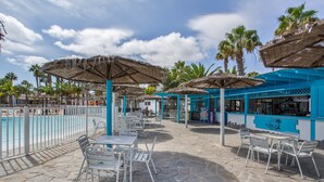 Een zwembadterras met buitenmeubilair, parasols en een bar.
