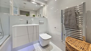 Un baño moderno con un inodoro blanco, un tocador con espejo y un perchero para toallas.