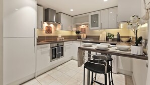 Cocina moderna con gabinetes blancos, campana extractora de acero inoxidable y una isla central con taburetes de bar.