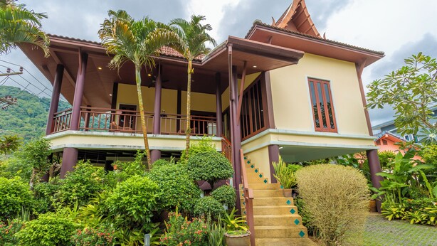 A traditional house with a balcony, surrounded by lush greenery and potted plants. - Thai-Style Villa with Charm V114 (Kamala)