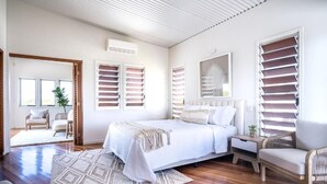 Une chambre à coucher moderne avec un grand lit, une table de chevet, une chaise et une fenêtre avec des stores.