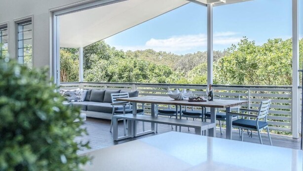 Une terrasse extérieure moderne, dotée d’un canapé, d’une table à manger et de chaises, et offrant une vue sur un paysage boisé.