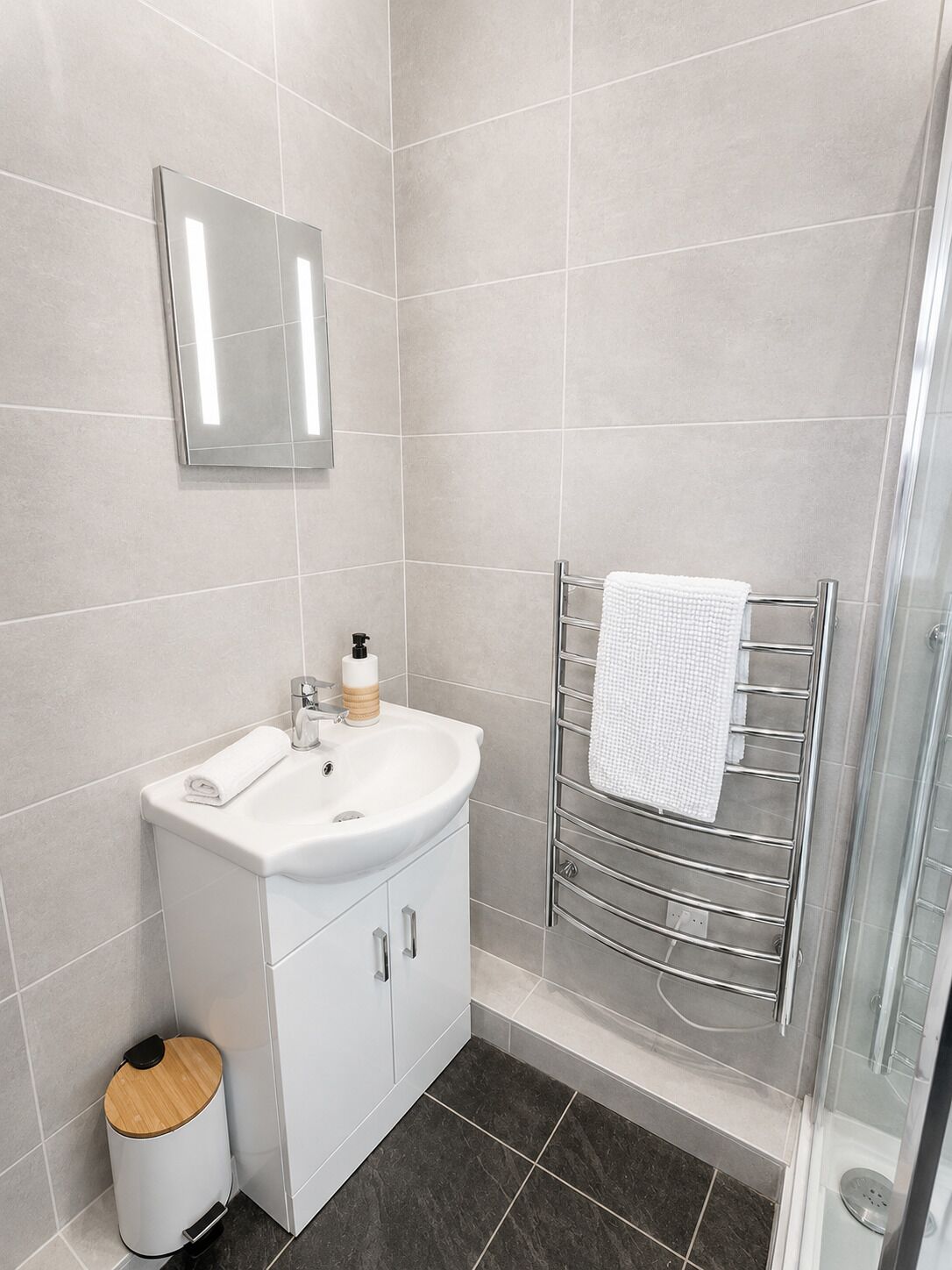 Un baño moderno con lavamanos, espejo y toallero blancos.