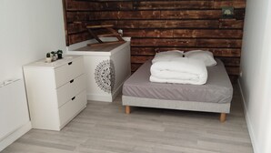 A bedroom with a wooden accent wall, a bed with a grey mattress, a white dresser, and a small clock on the wall. - Renovated apartment in quiet wine-growing village. 15min from Auxerre. (Irancy)