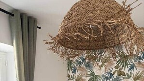 A bedroom with a bed, a woven hanging light fixture, a tropical leaf-patterned wallpaper, and a window with curtains. - La Parenthèse Douce (Saint-Brieuc)