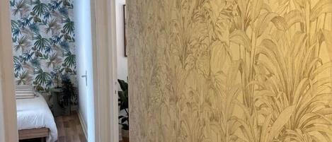 A hallway with a patterned wallpaper and a wooden floor.