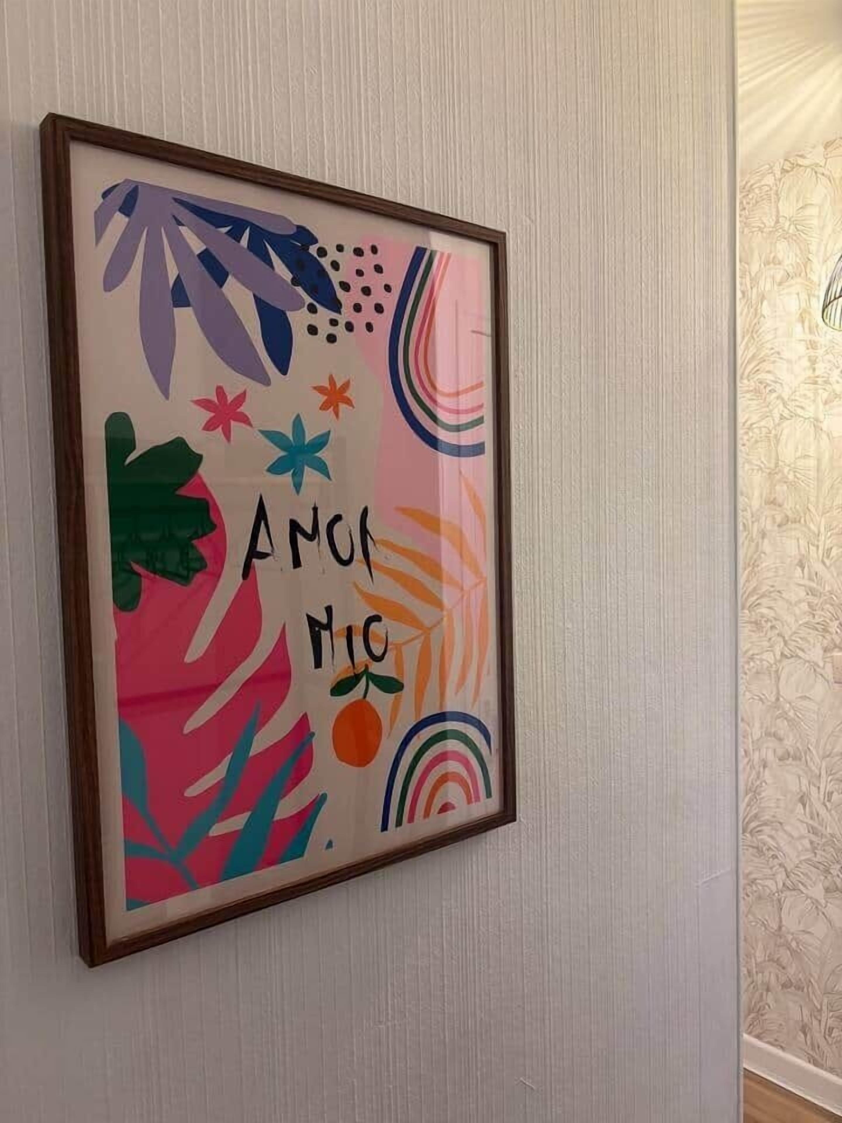 En inramad tavla med abstrakta motiv och texten ”AMON MOC” på en vägg.