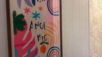 En inramad tavla med abstrakta motiv och texten ”AMON MOC” på en vägg.