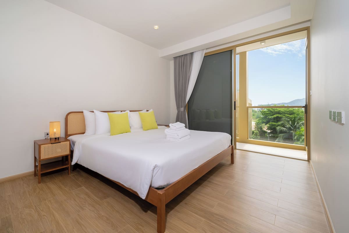 Une chambre avec un grand lit, une table de chevet avec une lampe et une vue sur la verdure grâce à une porte coulissante.