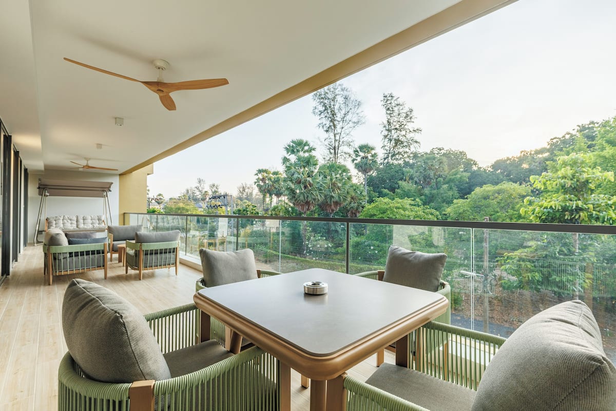 Un balcon avec une table et des chaises, un ventilateur de plafond et une vue sur une végétation luxuriante.